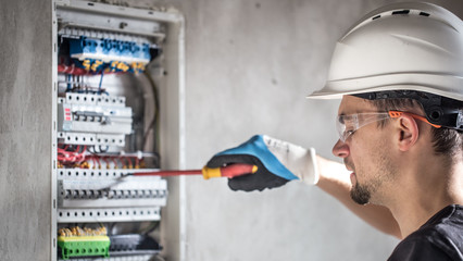 Man, an electrical technician working in a switchboard with fuses. Installation and connection of...