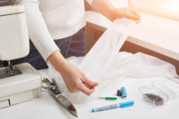 Female hands of a dressmaker. The girl uncovers a light fabric before sewing. Sewing machine and accessories in the image.