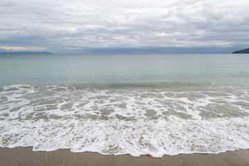 Long calm waves at sea on shore over cloudy sky