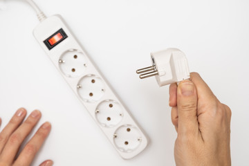 A hand holding a mains plug and trying to insert it into the main extension cord with many sockets