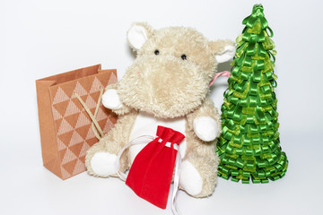 A teddy hippo in red santa hat sitting among christmas gifts and christmas tree, happy children holiday concept