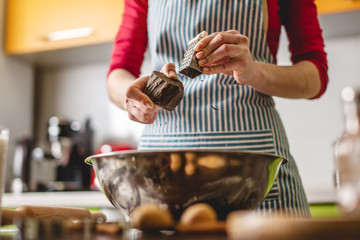 Cook housewife making cookies at home on a colorful kitchen. Woman rubbing on grater chocolate to prepare the dough