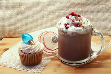 a cup of hot chocolate with whipped cream a chrismas ornament and a cupcake with a christmas light on top