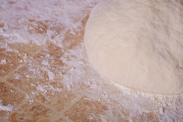 Prepared dough for baking pizza or bread on kitchen table with flour