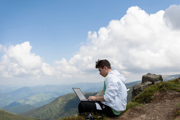 The guy sits on top of the mountain and works with a laptop