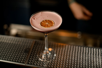Red cocktail with pink scum decorated with dried orange slice