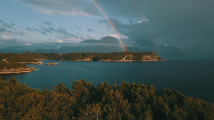The rainbow on a background of mountains, in the foreground a rock bay of a small town. Møre og Romsdal, Norway 2019