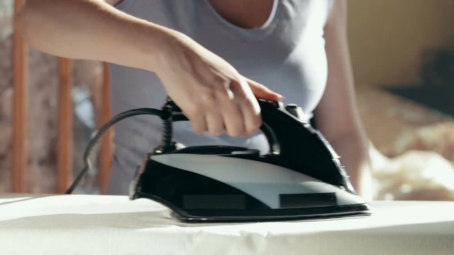 Pregnant woman ironing clothes on ironing board with a black iron close-up. Iron with steam and water stream.