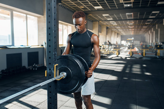 Muscular man in sportswear prepares barbell in gym