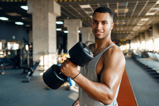Muscular man poses with heavy dumbbell in gym