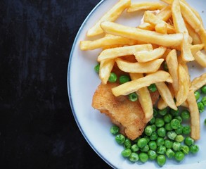 Fish and chips with green peas on a plate on dark grunge worn texture background with copy space.