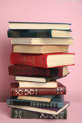 Stack of different hardcover books on pink background