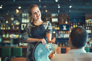 A girl waitre gets a tip from the client in the bar of the hotel. The girl in the vow. A bartender woman is happy to receive a tip at work. The concept of service. Emotions. The concept of service.   