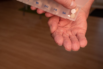 Hand mit Tablettendose leert Inhalt mit Tabletten in Hand einer älteren Person