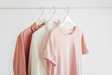 Feminine clothes in pastel pink  color on hanger on white background.  Elegant dresses and shirt....