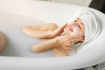 beautiful young woman with a towel on her head, lies in a bath with milk