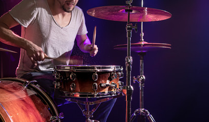 The drummer plays the drums. Beautiful blue and red background, with rays of light. Beautiful special effects smoke and lighting. The process of playing a musical instrument. Close-up photo.