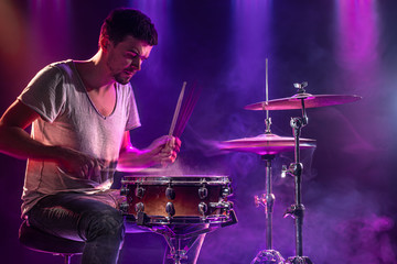 The drummer plays the drums. Beautiful blue and red background, with rays of light. Beautiful special effects smoke and lighting. The process of playing a musical instrument. Close-up photo.