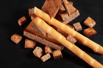 Rye crackers and salty sticks, stacked on a slide, on a dark board.