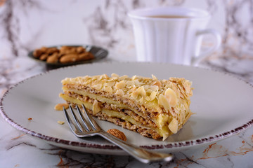 A portion of almond cake in a ceramic plate on the table next to cup of tea
