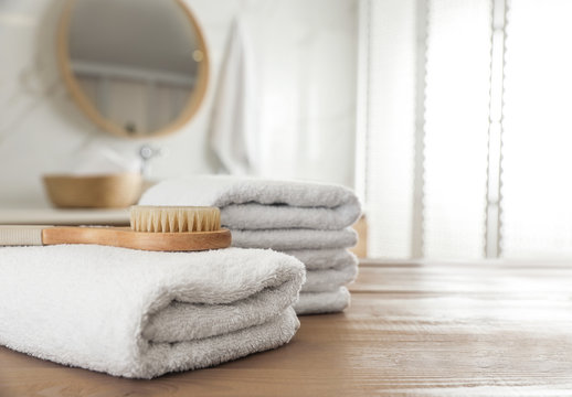 Stack of clean towels and massage brush on wooden table in bathroom. Space for text
