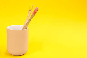 Toothbrushes made of bamboo in holder on yellow background. Space for text