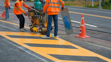 Road workers in reflective vests with thermoplastic spray road marking machine are working to paint...
