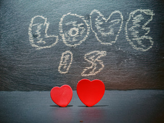Two red hearts side by side and chalk sign love is in the background. Saint Valentine abstract background.