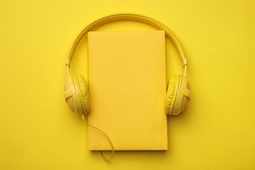 Book and modern headphones on yellow background, top view