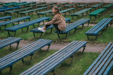 Lonely sad teenager sitting alone on a bench in public place with multiple rows of desolate benches