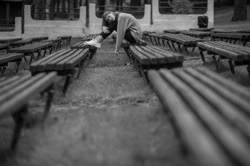 Obraz premium Lonely sad teenager sitting alone on a bench in public place with multiple rows of desolate benches