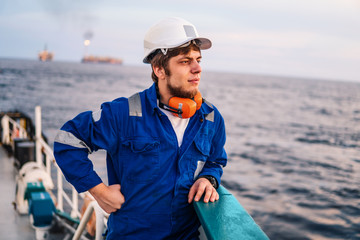 Marine Deck Officer or Chief mate seaman on deck of offshore vessel or ship , wearing PPE personal protective equipment - helmet, coverall looks at sea. ocean view
