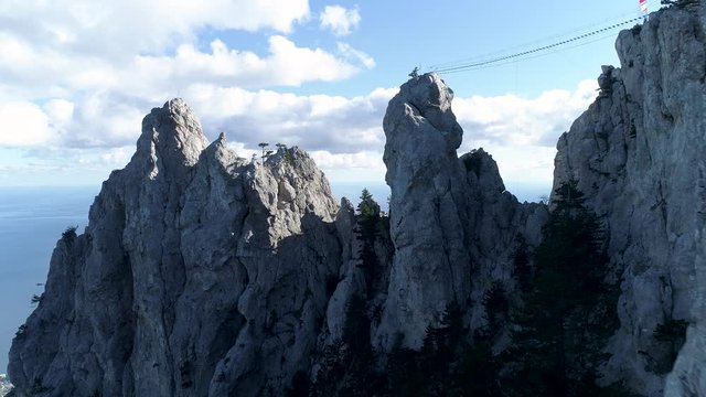 Suspension bridge on the mountain peak with the blue ocean and cloudy sky on the background. Shot. Amazing aerial view of the sea coast with rope bridge over the rocks.