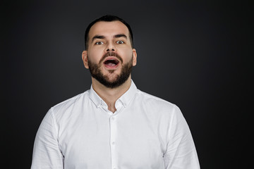 Obraz premium Portrait of young surprised handsome bearded man with shocked facial expression on black background