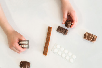Child holds in one hand a package of pills and chocolate candy in the second hand. Concept of the...