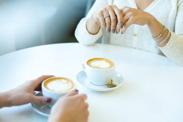 Hands of two young friendly women in casualwear having coffee at break in cafe
