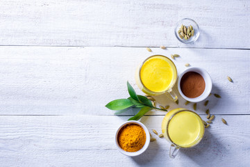 Two glass cups with golden latte, turmeric, cardamom and cinnamon on a white wooden background.