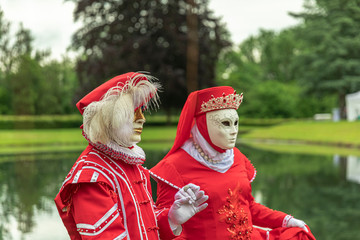Couple standing in masks and red masquerade costumes during Venetian carnival in Annevoie  gardens, Rue des jardins, 37 a, Annevoie/ Belgium - 311239009