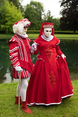 Couple standing in masks and red masquerade costumes during Venetian carnival in Annevoie  gardens, Rue des jardins, 37 a, Annevoie/ Belgium - 311239022