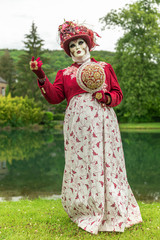 A woman standing in mask and red masquerade costume agains the pond background - 311239084