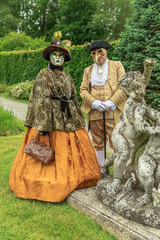 Couple standing in masks and orange masquerade costumes during Venetian carnival in Annevoie  gardens, Rue des jardins, 37 a, Annevoie/ Belgium - 311239434