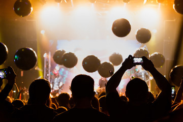 Silhouettes of crowds of spectators at a concert with smartphones in their hands.