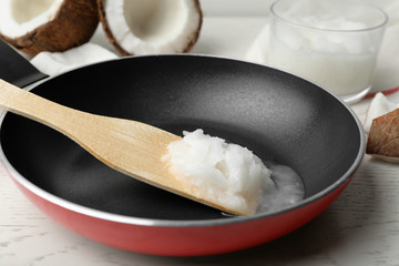 Frying pan with coconut oil and wooden spatula on white wooden table, closeup. Healthy cooking