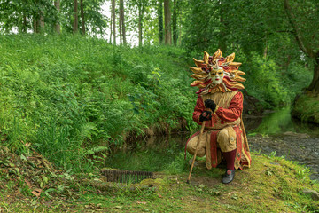 A man standing in mask and red masquerade costume agains the pond background - 311239607