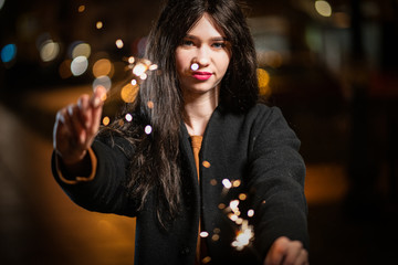 beautiful girl with sparklers in the evening on the street. festive mood sparkling hand-held fireworks.