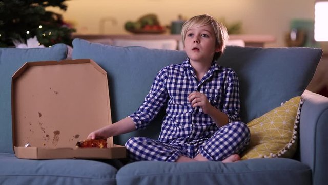 cute boy, kid watches horror movie and eats pizza on the couch at night