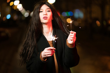 beautiful girl with sparklers in the evening on the street. festive mood sparkling hand-held fireworks.