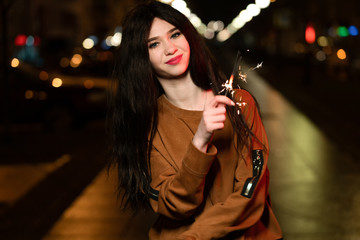 beautiful girl with sparklers in the evening on the street. festive mood sparkling hand-held...