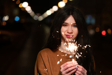 beautiful girl with sparklers in the evening on the street. festive mood sparkling hand-held fireworks.