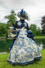 A woman standing in mask and blue masquerade costume agains the pond background - 311240098